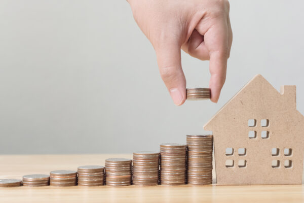 Hand plaatst stapel munten naast huisje