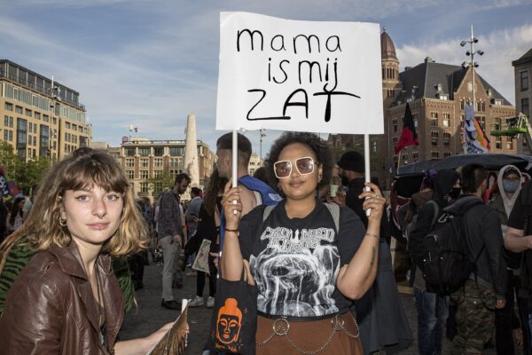 Jonge actievoerders staan op de dam in Amsterdam tijdens een woonprotest. In hand een bord met de tekst 'mama is mij zat'.